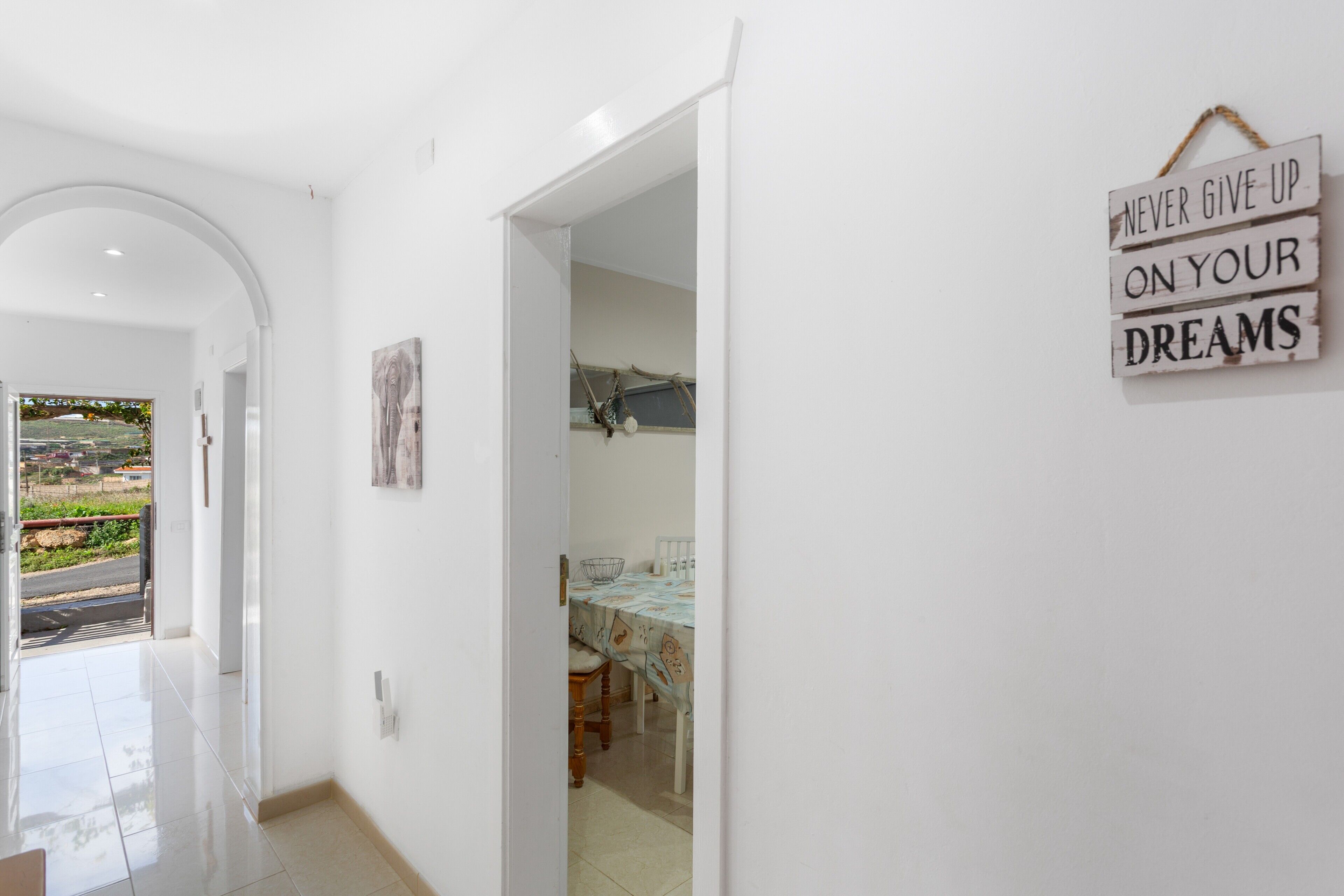 A hallway with a dining area, a view through an open door, and a motivational sign on the wall.