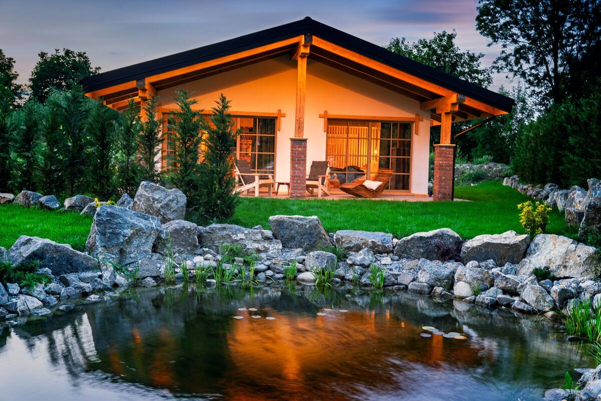 Une maison moderne dotée d’une grande véranda à l’avant, d’un étang et d’une pelouse bien entretenue.