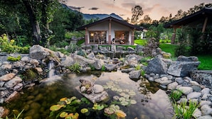 A house with a pond, surrounded by rocks and plants. - Thomhof Chalets (Bran)