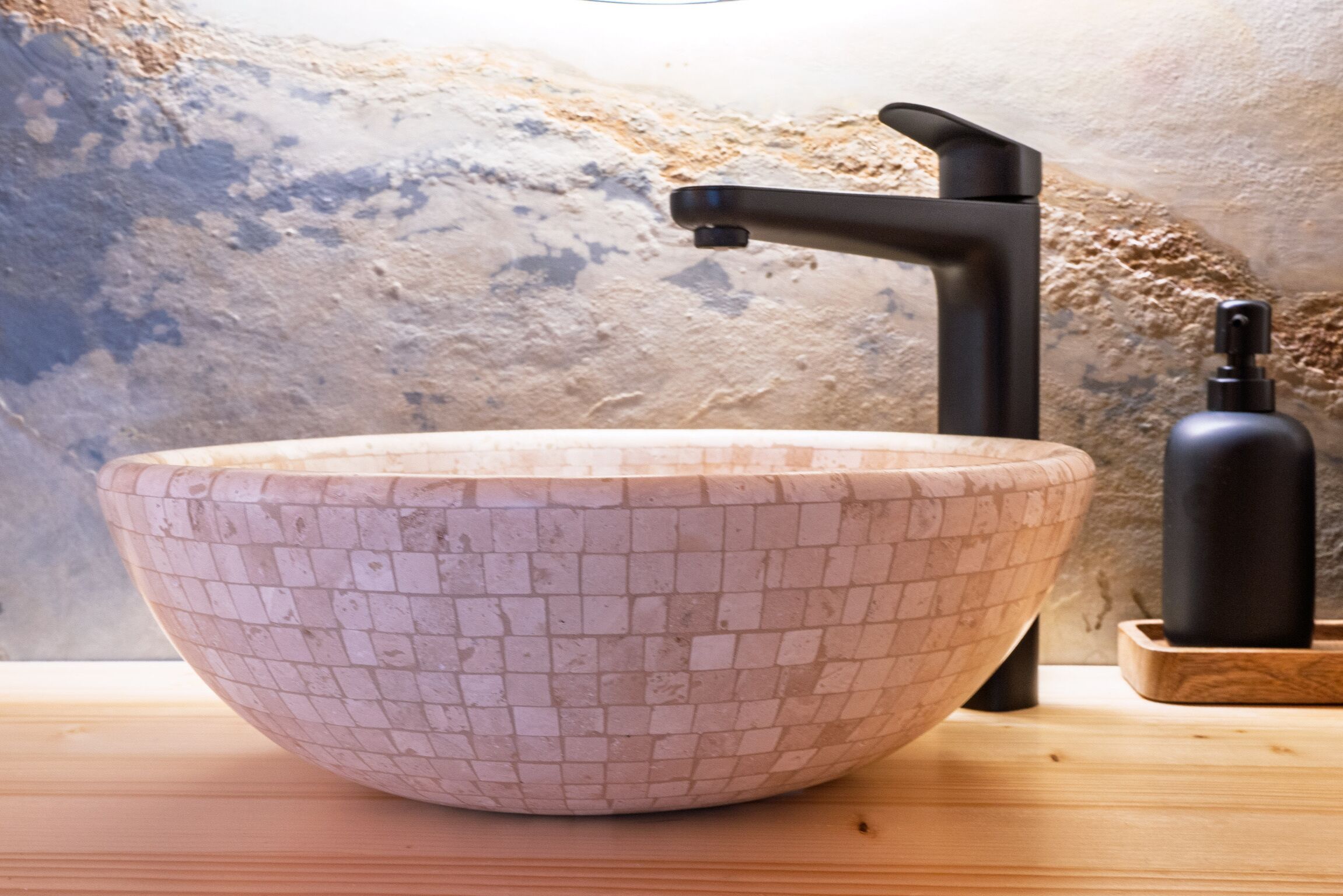 A mosaic bowl sink with a black faucet on a wooden surface.