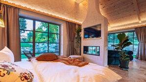 A bedroom with a large bed, a TV mounted on the wall, and a potted plant. - Thomhof Chalets (Bran)