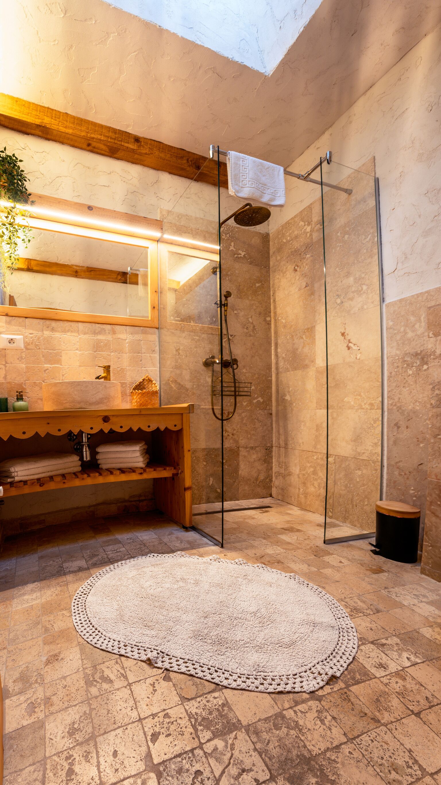 A modern bathroom with a stone shower, a wooden vanity, and a large, round, crocheted rug.