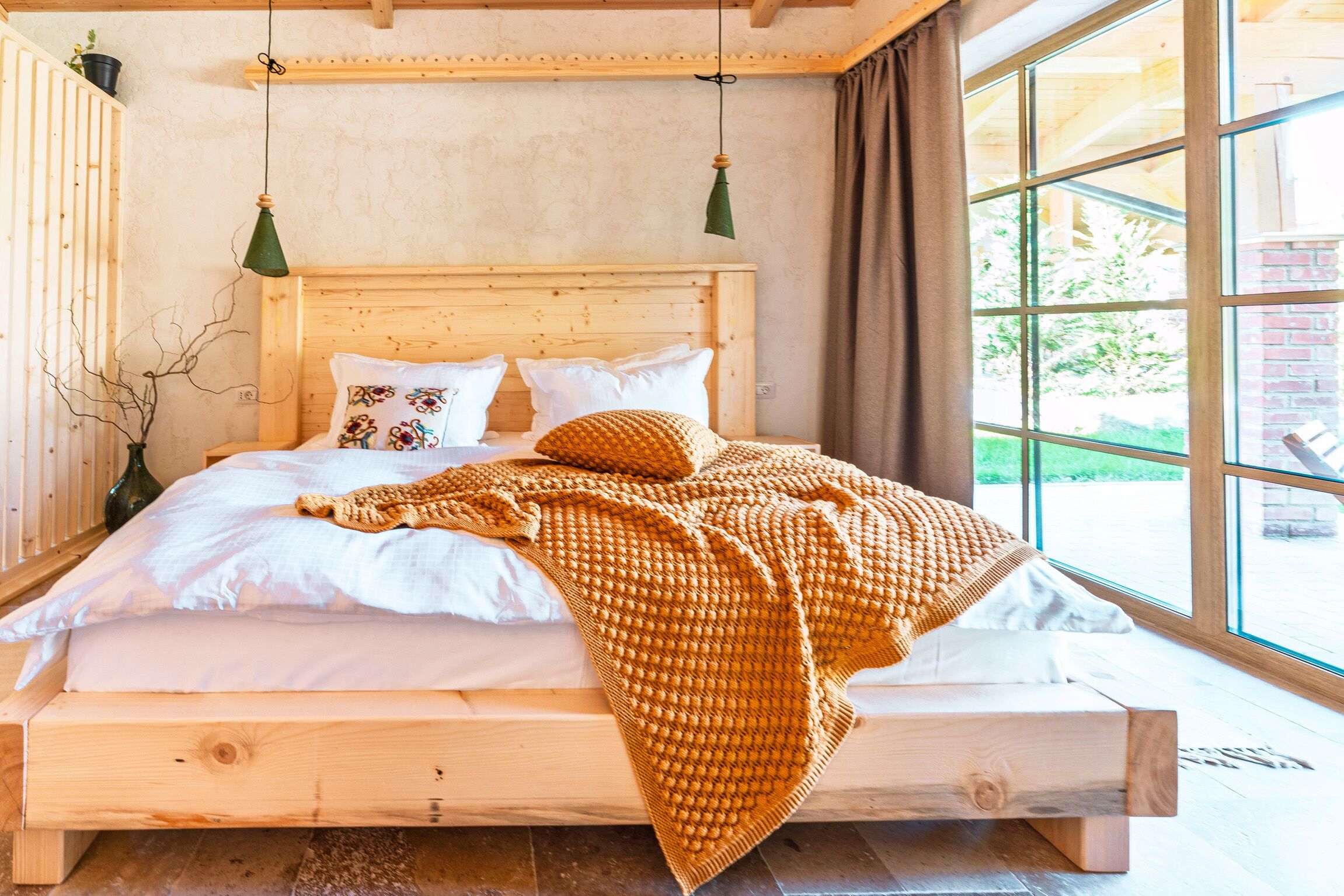 Een houten bed met een wit-oranje deken, houten hoofdeinde en twee groene hanglampen.