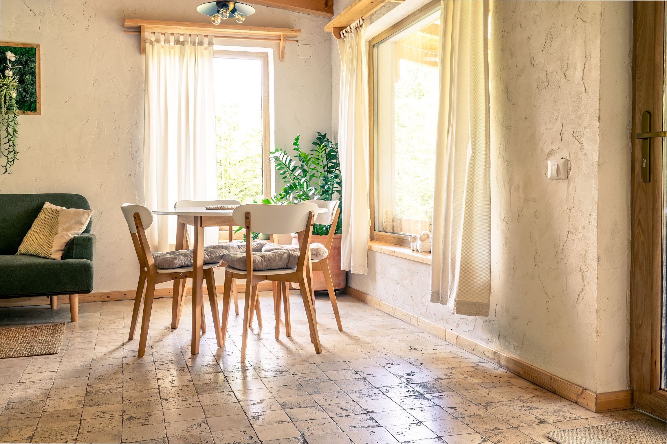 Un rincón comedor acogedor con una mesa y sillas, un sofá verde y una planta en maceta.