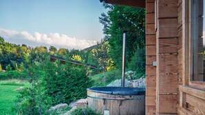 A wooden deck with a hot tub and a view of a lush garden and hills. - Thomhof Chalets (Bran)