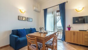 Una sala de estar acogedora con una mesa de comedor de madera, un sofá azul y un televisor montado en la pared.