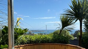 A hot tub with a wooden edge, surrounded by greenery and a clear view of the ocean. - Ocean View Hot Tub Suites (Pichilemu)