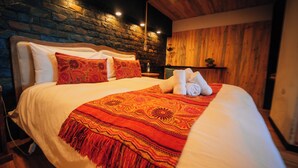 A neatly made bed with a patterned blanket and pillows, a wooden headboard, and a stone wall. - Ocean View Hot Tub Suites (Pichilemu)