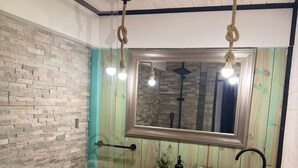 A bathroom with a wooden vanity, a stone sink, a mirror, and a shower with a glass door. - Ocean View Hot Tub Suites (Pichilemu)