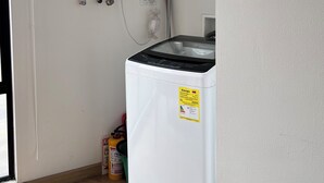 A laundry room with a white washing machine, a water heater, and a metal rack on the wall. - San Felipe (Bogotá)