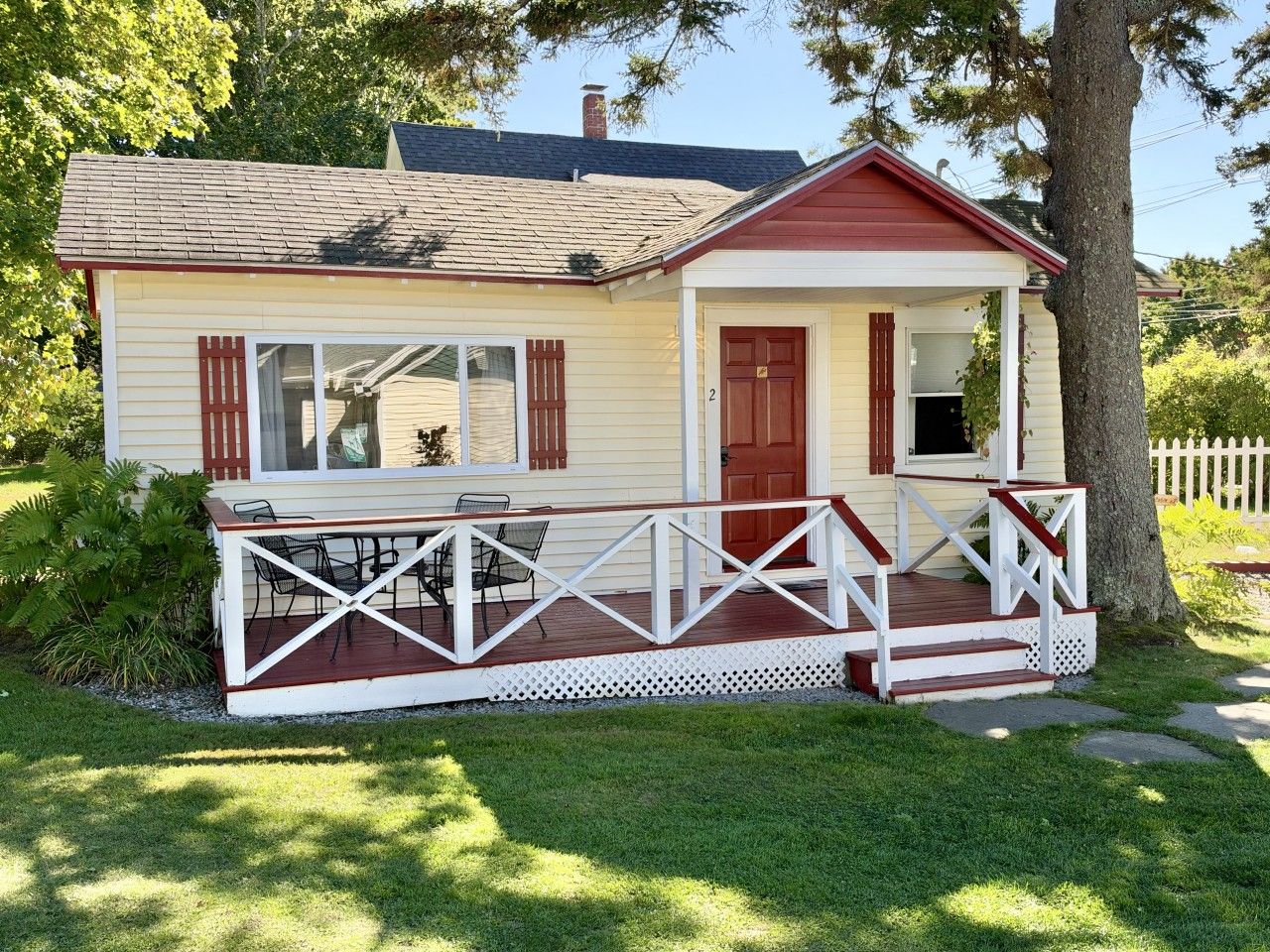 Ein eingeschossiges Haus mit Veranda, einer roten Tür und der Hausnummer 2.