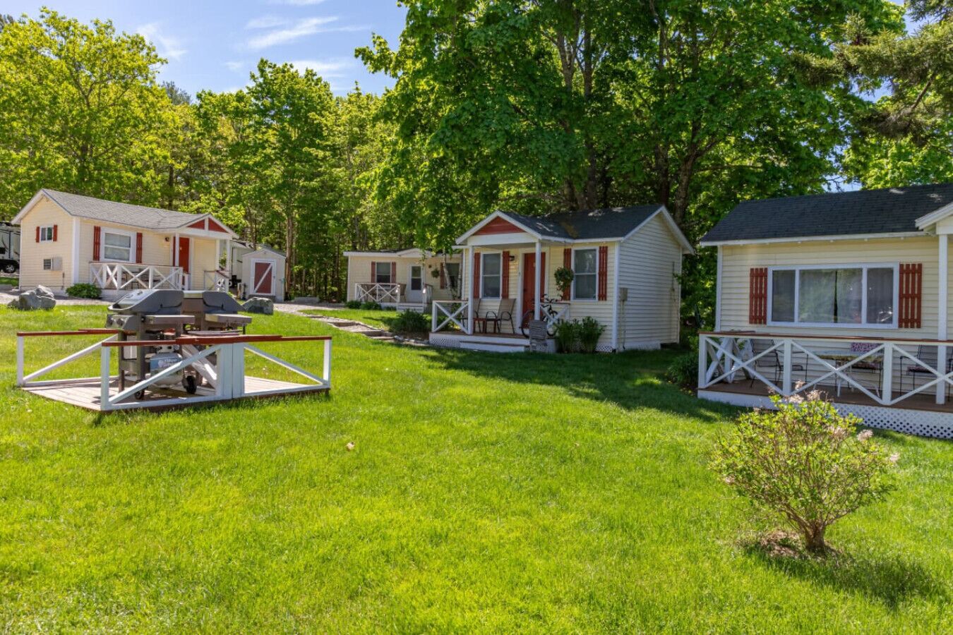 A row of mobile homes with a grassy yard and a barbecue setup.