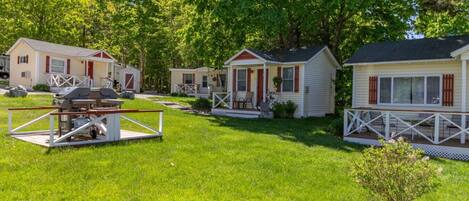 A row of mobile homes with a grassy yard and a barbecue setup.
