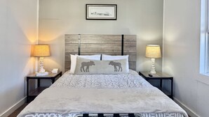 Una cama bien tendida con ropa de cama estampada, dos mesitas de noche con lámparas y un cuadro en la pared.