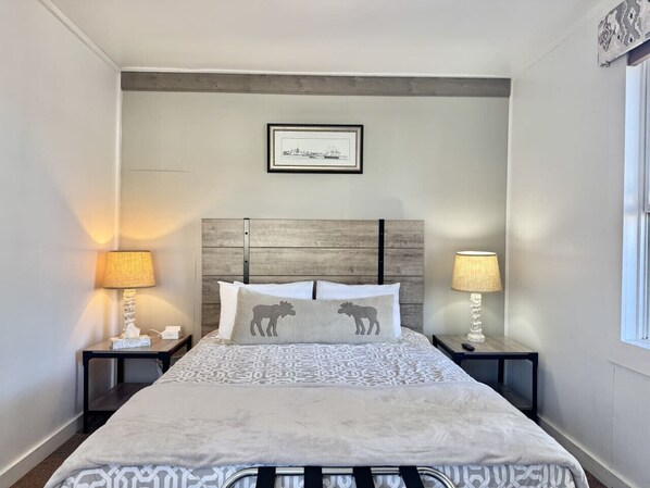A neatly made bed with patterned bedding, two bedside tables with lamps, and a framed picture on the wall.