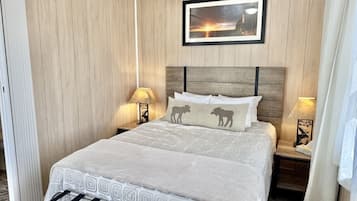 A hotel room with a wooden paneled wall, a bed with a patterned bedspread, two bedside lamps, and a framed picture above the bed.