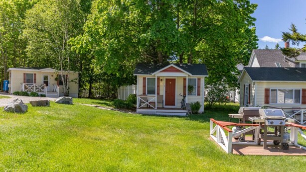 A small, single-story house with a front porch, a covered outdoor grill, and a well-maintained lawn. - Gallagher`s Travels Cabin 3 (Single Queen) (Bar Harbor)