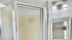 A bathroom with a shower enclosure, a toilet, a sink with a mirror, and a towel hanging on the wall. - Gallagher`s Travels Cabin 3 (Single Queen) (Bar Harbor)