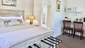A bedroom with a bed, bedside table, lamp, and a desk with a chair. - Gallagher`s Travels Cabin 3 (Single Queen) (Bar Harbor)