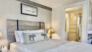 A neatly arranged hotel room with a large bed, a bedside table with a lamp, and a framed picture on the wall.
