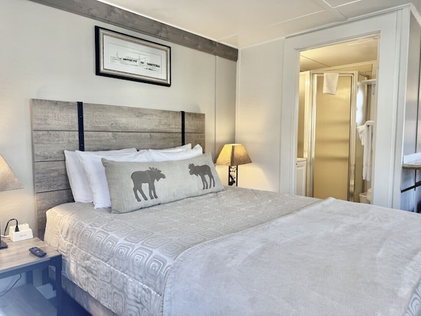 Habitación de hotel impecable con una cama grande, una mesita de noche con lámpara y un cuadro enmarcado en la pared.