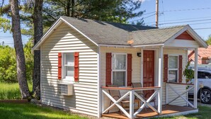 A small, single-story cabin with a porch, a small attached garage, and a well-maintained lawn.