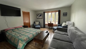 A room with a bed, two armchairs, a sofa, a wooden coffee table, and a television.