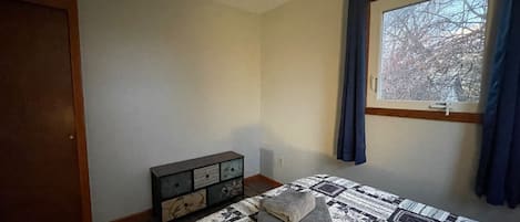 A bedroom with a bed, a dresser, a window with curtains, and a door.
