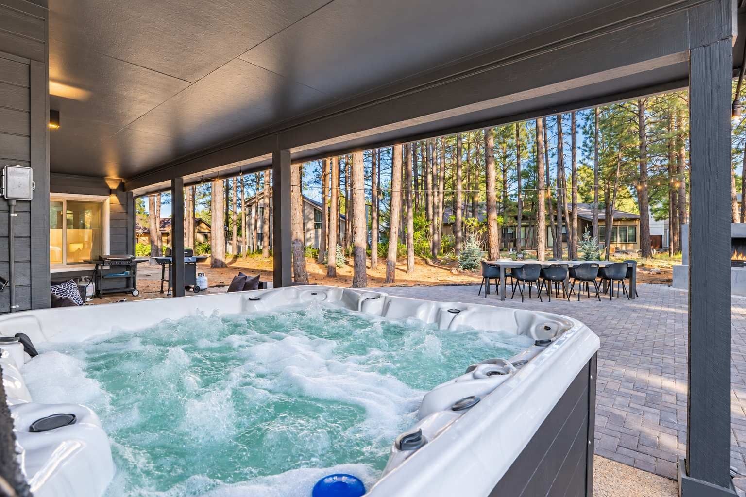 A hot tub area with a view of a forest and a patio with chairs and a table.