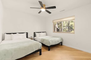 Une chambre avec deux lits, un ventilateur de plafond, une fenêtre donnant sur des arbres et un plancher en bois.