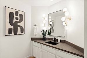 Une salle de bain avec un grand miroir, un meuble-lavabo, un évier et une plante en pot.