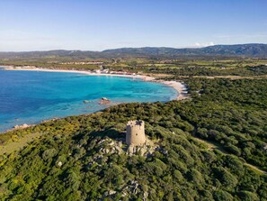 Kustlandschap met een toren op een heuvel, helderblauwe zee en groene heuvels op de achtergrond.