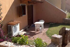 Un patio con una mesa y sillas blancas, un equipo de aire acondicionado blanco y un muro de piedra.