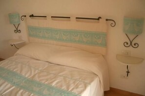 A bedroom with a bed, a bedside table, a wall-mounted shelf, and decorative wall art. - Your Green Retreat by the sea (Aglientu)