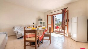 A small, well-lit room with a dining table set for two, a sofa, a small cabinet, and a refrigerator. - San Teodoro Flat Steps From the Beach (San Teodoro)