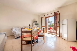A small, well-lit room with a dining table set for two, a sofa, a small cabinet, and a refrigerator. - San Teodoro Flat Steps From the Beach (San Teodoro)