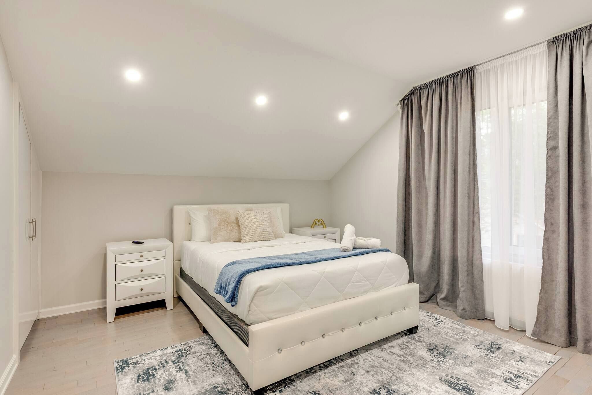 A bedroom with a bed, nightstand, and a window with curtains.