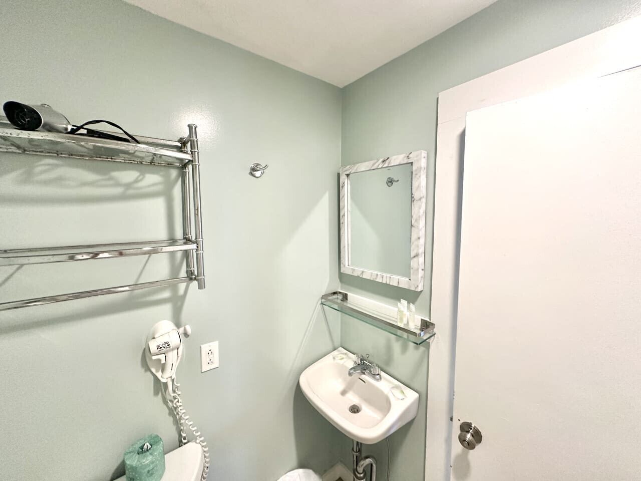 A bathroom with a white sink, a mirror with a marble frame, and a hairdryer on a metal shelf.