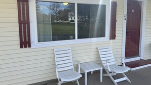 A house with a large window, two white chairs, and a red door. - Gallagher`s Travels Room 12-A (King Bed) (Bar Harbor)