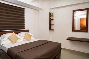 A hotel room with a bed, a wooden headboard, a bedside shelf with flowers, a mirror, and a wooden bench. - H2o Residences Colombo (Colombo)