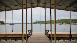 A wooden dock leading to a covered area with a view of a lake and distant buildings. - Water front cabin #12 Cabin in Graham, steps from Possum Kingdom Lake (Graham)