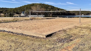A sandy volleyball court with a metal fence, a bench, and a small building in the background. - Water front cabin #12 Cabin in Graham, steps from Possum Kingdom Lake (Graham)