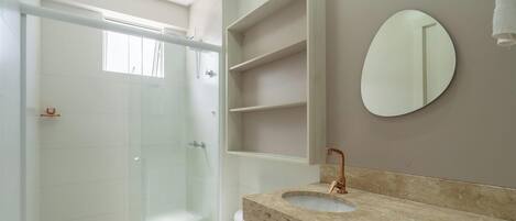 A bathroom with a glass shower enclosure, a sink with a copper faucet, and a mirror.