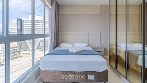 A modern hotel room with a large window, a bed with white linens, a bedside table, and a wardrobe with a mirror. - Apartment Sea View 500 m From the Beach Roo0401 (Itapema)