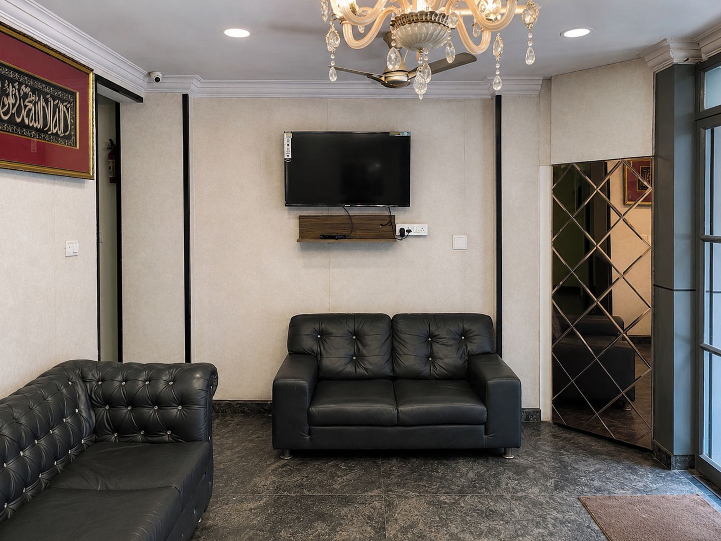 Una sala de estar moderna con un televisor de pantalla plana montado en la pared, un sofá de cuero negro y un sillón a juego.