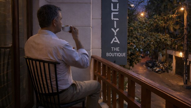 A man sitting on a chair outside a building with a sign that reads "LUIYA THE BOUTIQUE". - Luciya The Boutique Hotel (Bengaluru)