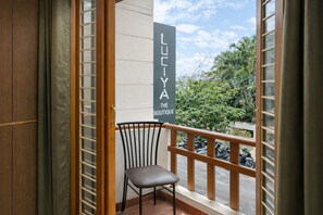Ein Balkon mit einem Stuhl, einem Schild mit der Aufschrift 'LUTYA THE BOUTIQUE' und Blick auf abgestellte Roller und Grünflächen.