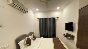 A hotel room with a bed, air conditioning unit, curtains, a television, and a ceiling fan. - Luciya The Boutique Hotel (Bengaluru)