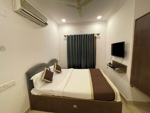 Une chambre d’hôtel équipée d’un lit, d’un climatiseur, de rideaux, d’une télévision et d’un ventilateur de plafond.