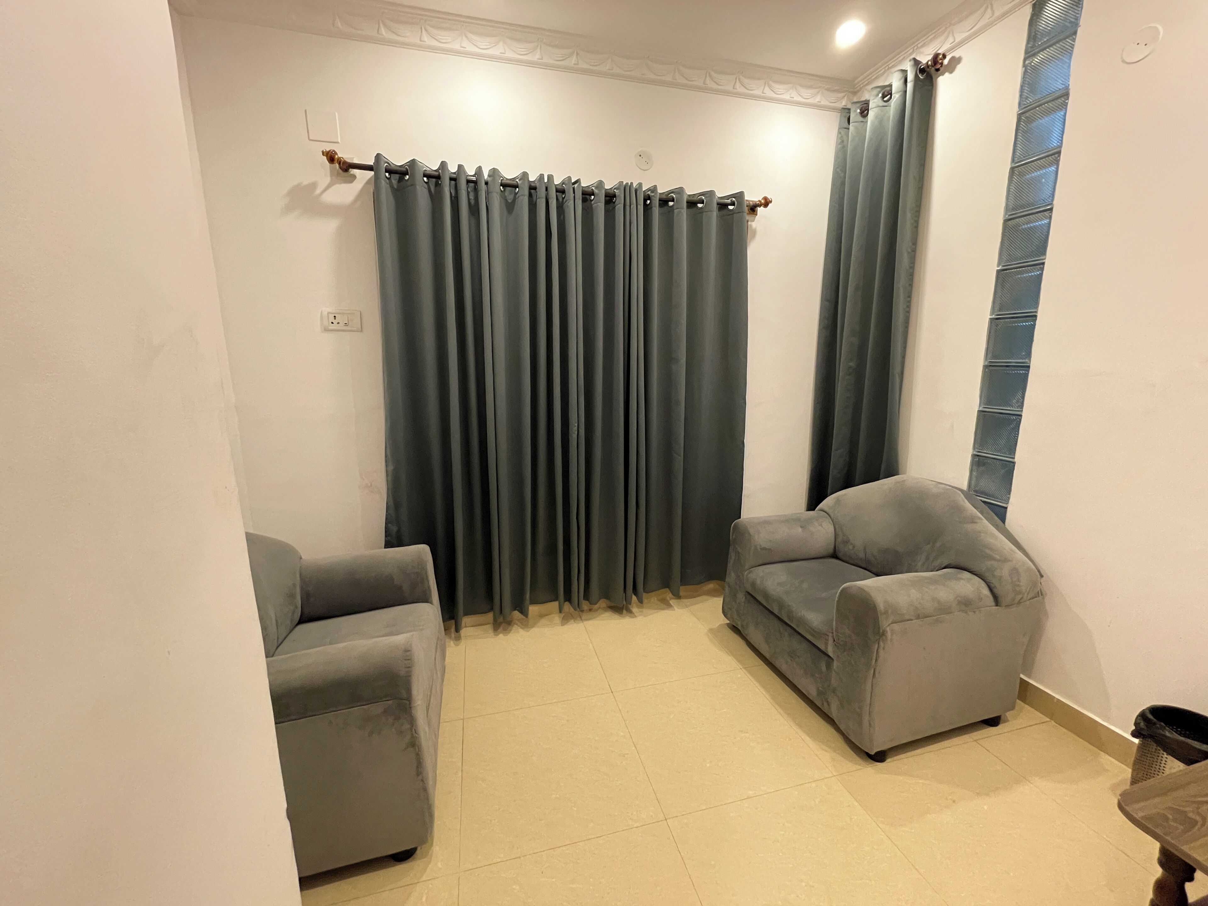 A room with two grey armchairs, a dark curtain, and a tiled floor.